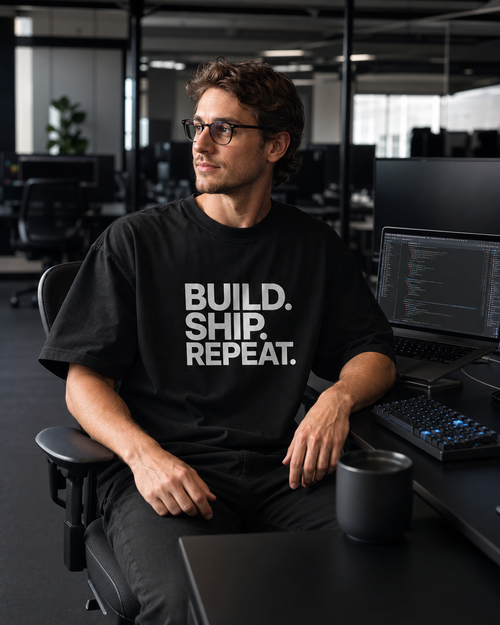Person wearing a black t-shirt with 'BUILD. SHIP. REPEAT.' text in an office setting.