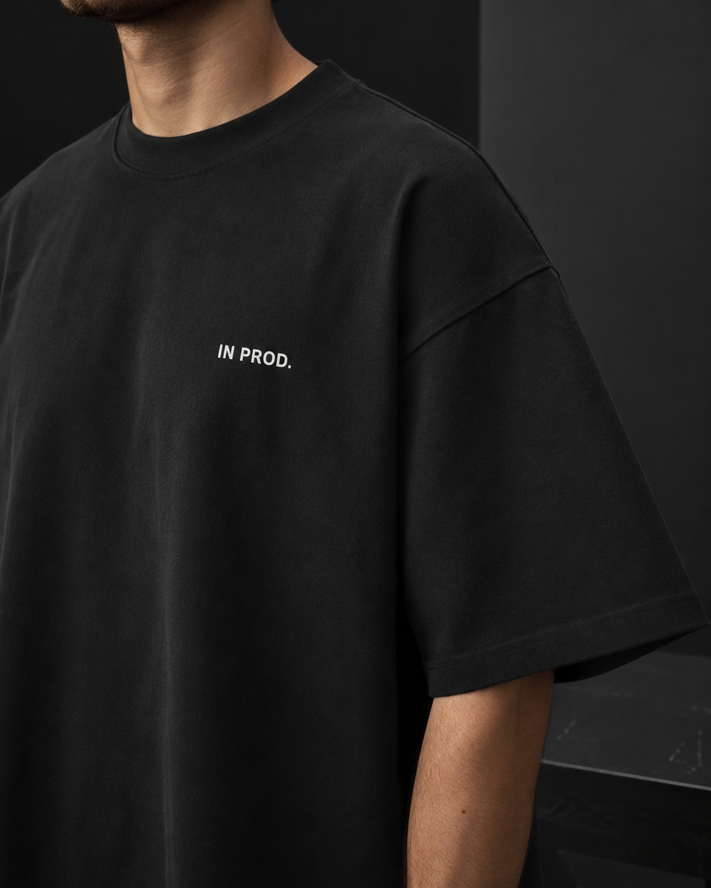 Person wearing a black t-shirt with 'IN PROD.' text on a dark background