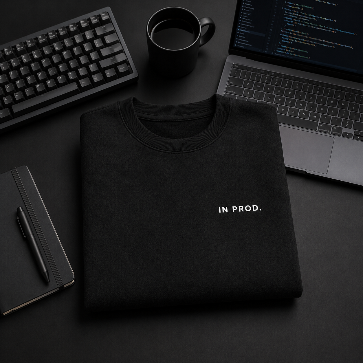 Black sweatshirt with 'IN PROD.' text on a dark desk with laptop, keyboard, and mug.