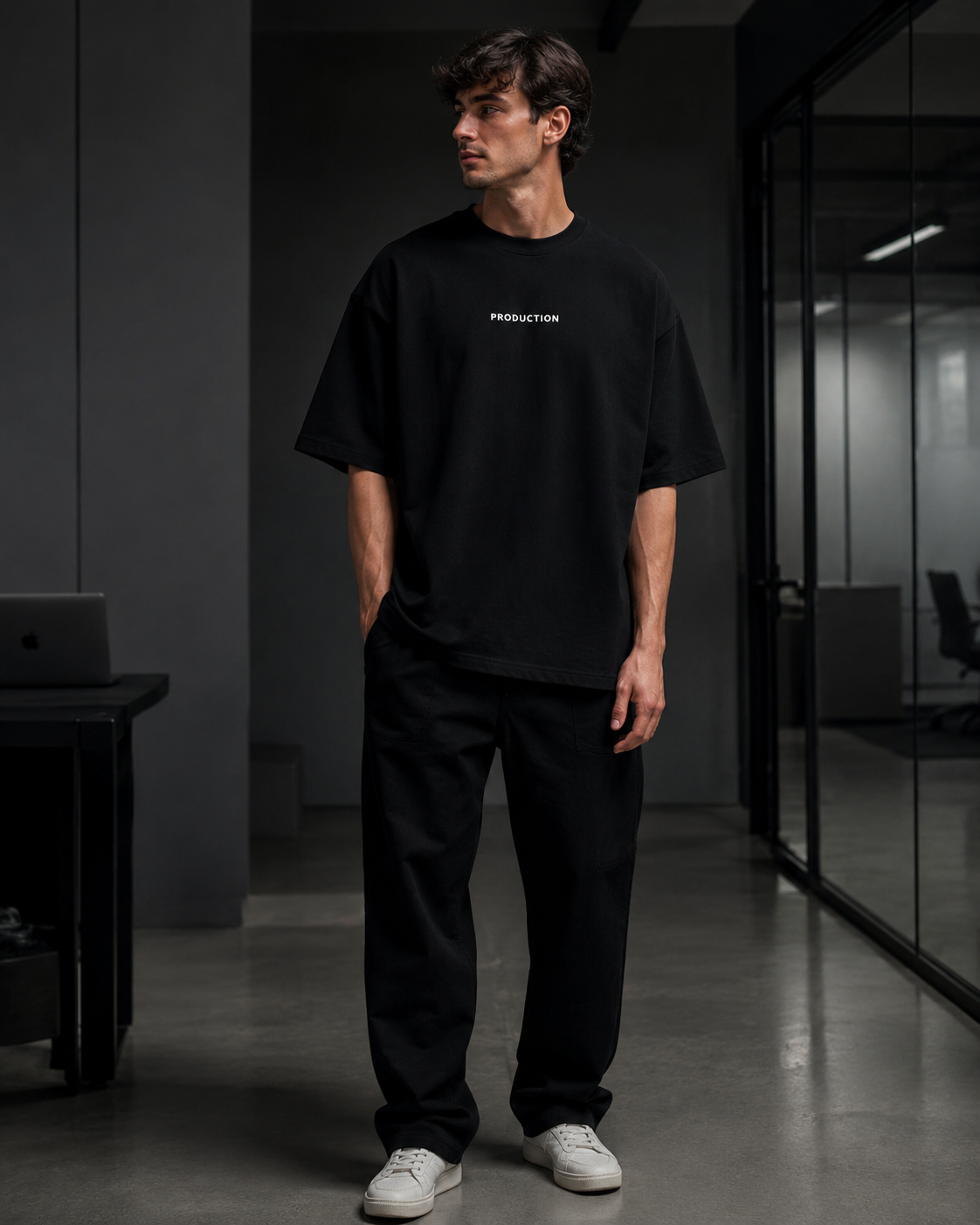 Person wearing a black t-shirt with 'PRODUCTION' text in a modern office setting